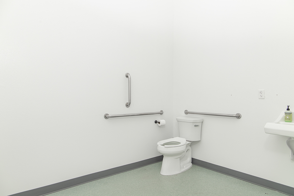 Commercial ADA-compliant bathroom with tile flooring, accessible sink, grab bars, and standard fixtures.