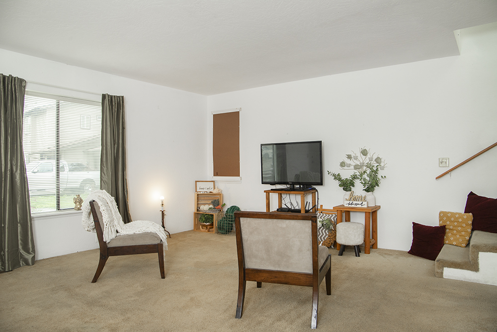 Bright living room with carpet flooring, large front-facing window, and open layout.
